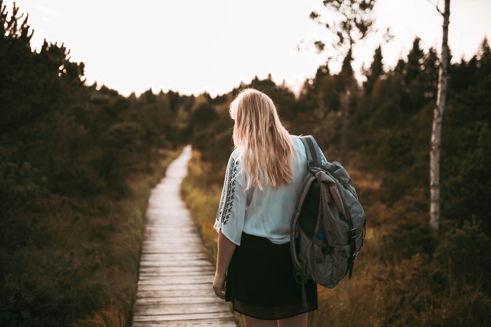 back of woman standing on pathway carrying backpack